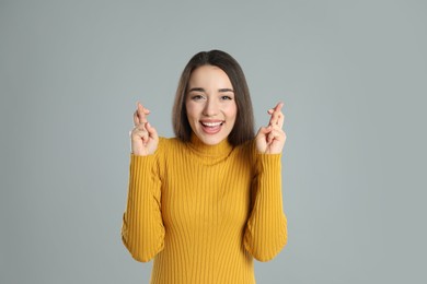 Photo of Excited young woman holding fingers crossed on grey background. Superstition for good luck