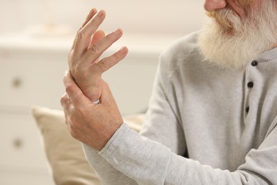 Photo of Senior man suffering from pain in hand indoors, closeup. Rheumatism symptom