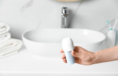 Photo of Woman holding roll-on deodorant in bathroom, closeup view. Space for text