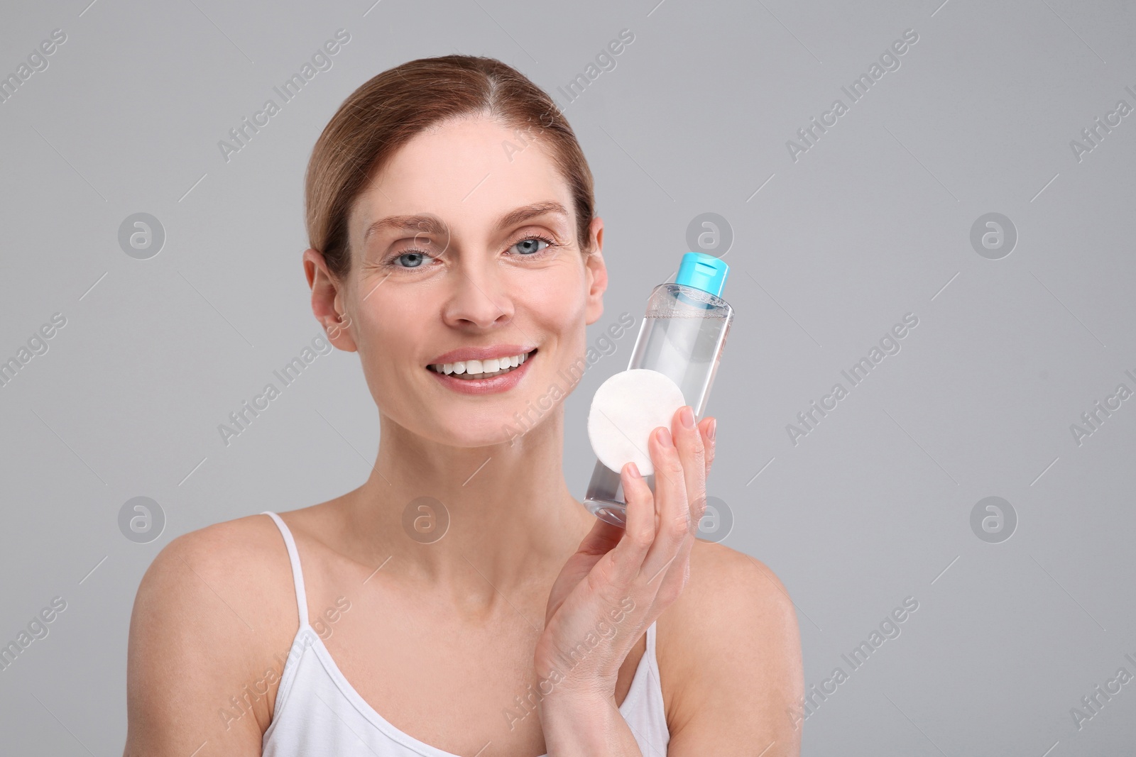 Photo of Beautiful woman with makeup remover and cotton pad on gray background, space for text