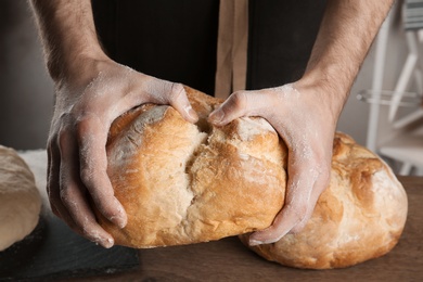 Male baker holding loaf of bread over table, closeup