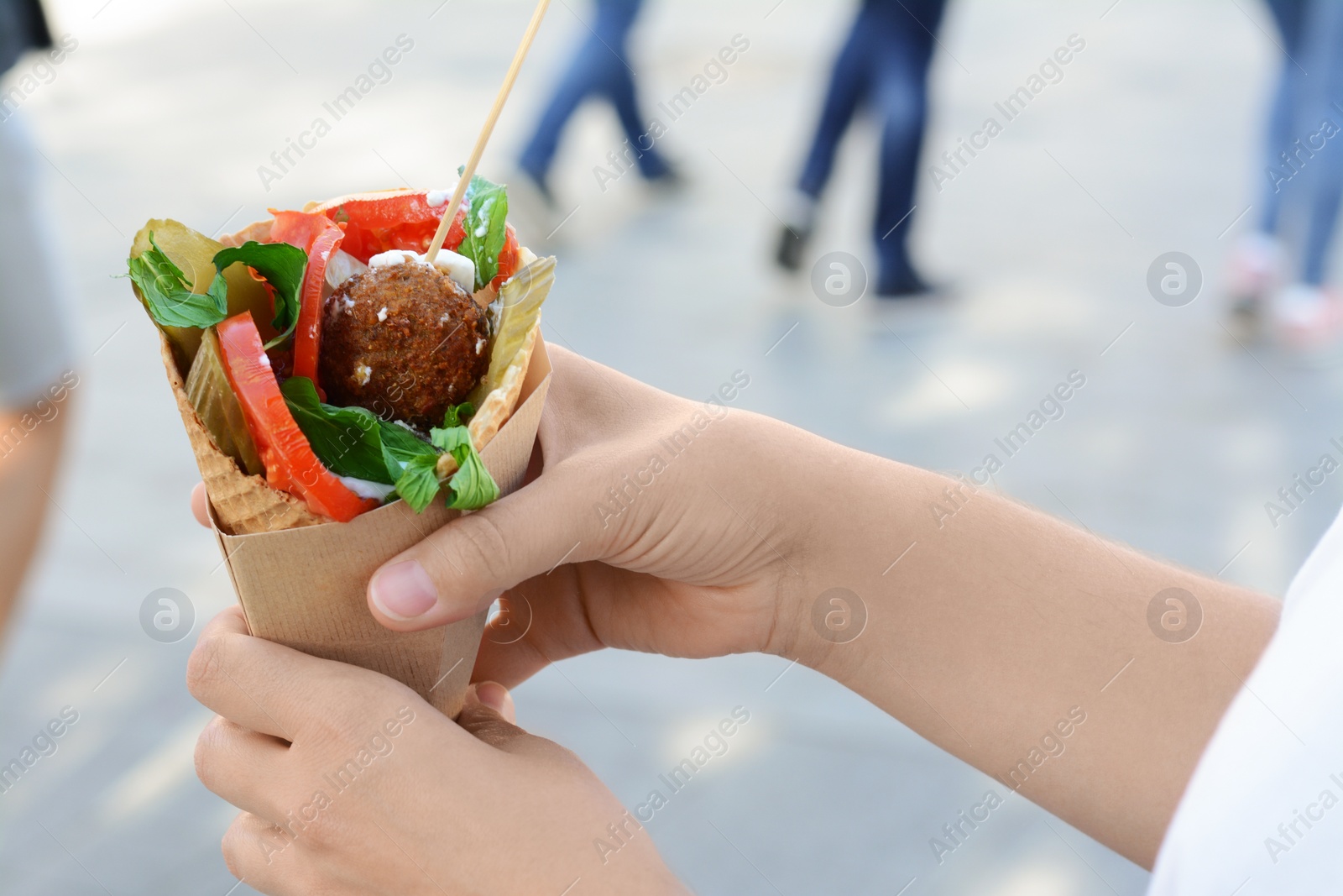 Photo of Woman holding wafer with falafel and vegetables outdoors, closeup. Street food