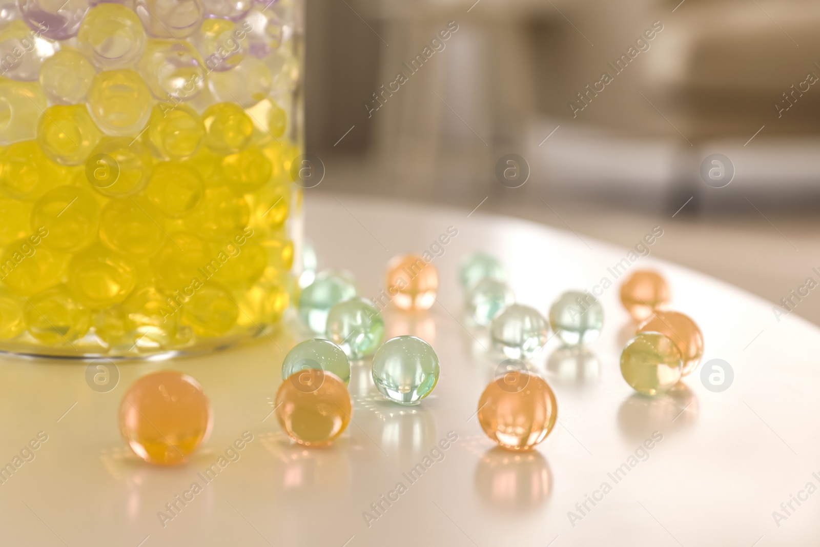 Photo of Different color fillers and glass vase on white table in room, closeup. Water beads