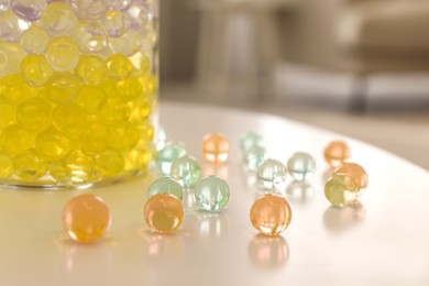 Photo of Different color fillers and glass vase on white table in room, closeup. Water beads