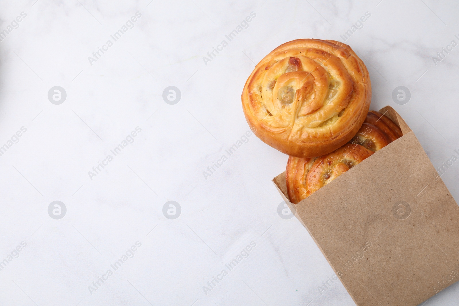 Photo of Paper bag with delicious rolls on white marble table, top view and space for text. Sweet buns