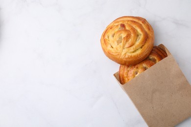 Photo of Paper bag with delicious rolls on white marble table, top view and space for text. Sweet buns