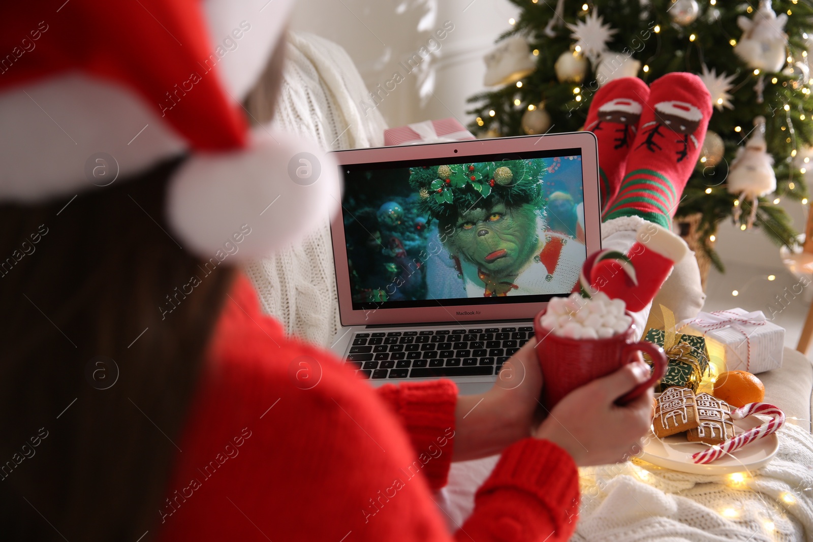 Photo of MYKOLAIV, UKRAINE - DECEMBER 25, 2020: Woman with sweet drink watching The Grinch movie on laptop at home, closeup. Cozy winter holidays atmosphere