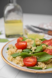 Delicious quinoa salad with tomatoes and spinach leaves served on white tiled table, closeup