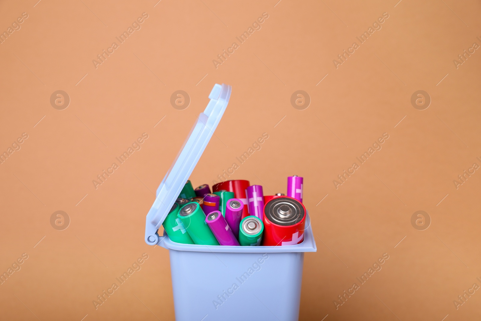 Photo of Many used batteries in recycling bin on coral background