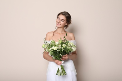 Young bride wearing wedding dress with beautiful bouquet on beige background