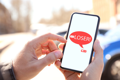 Image of Man receiving offensive message with text LOSER!, closeup. Cyber bullying concept