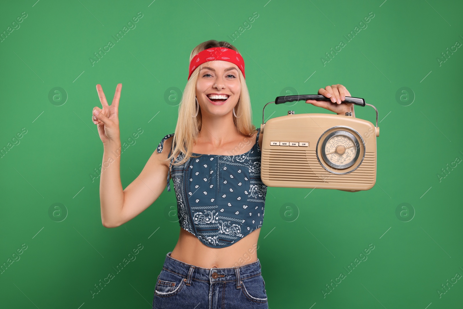 Photo of Happy hippie woman with retro radio receiver showing peace sign on green background