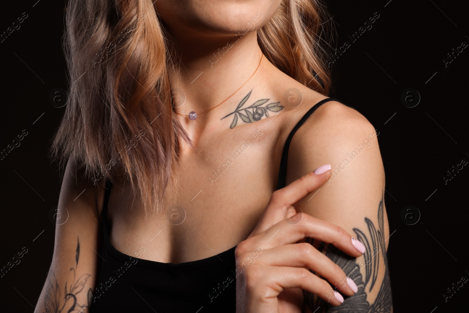 Photo of Beautiful woman with tattoos on body against black background, closeup