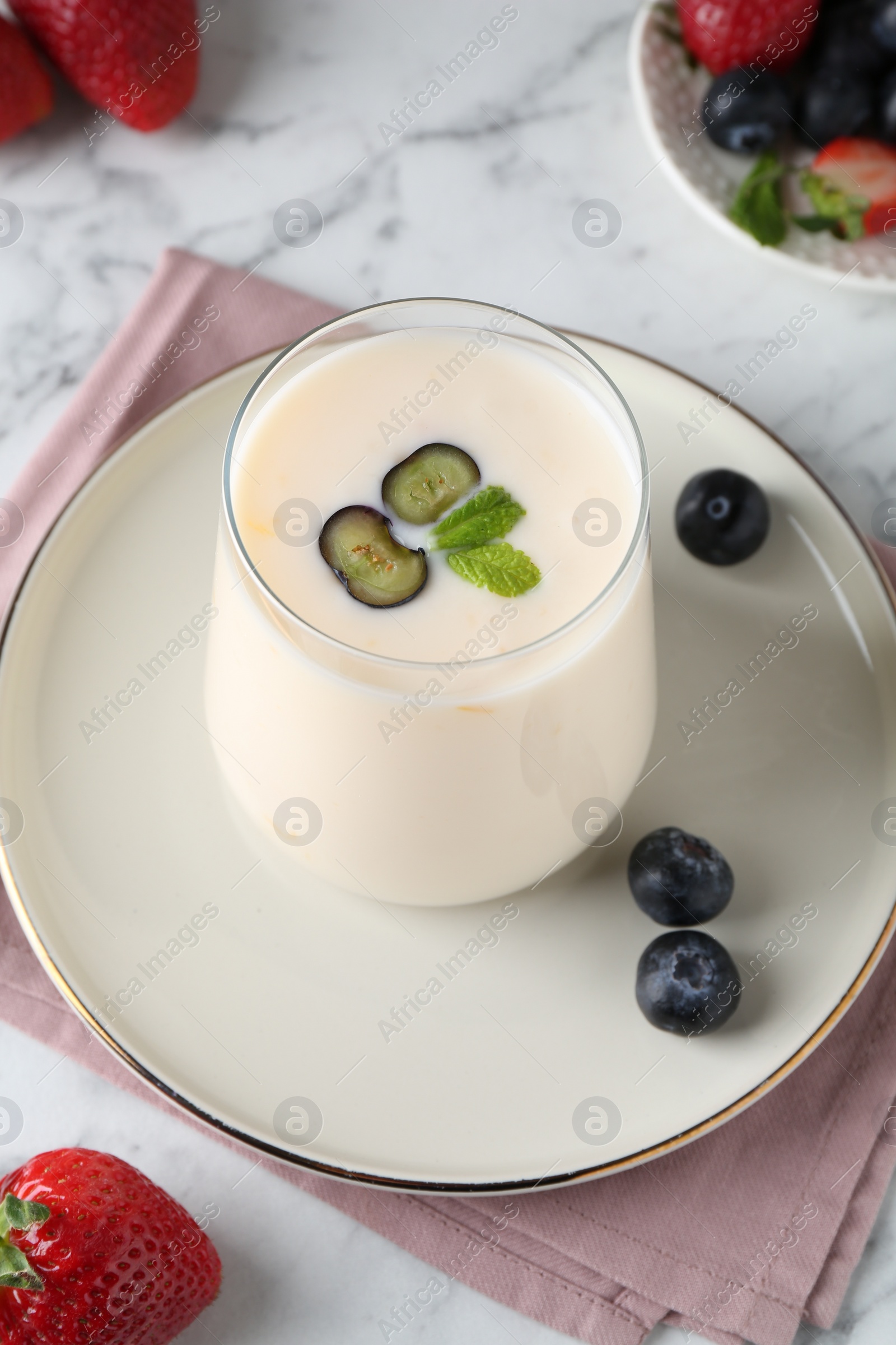 Photo of Tasty yogurt in glass and berries on white marble table