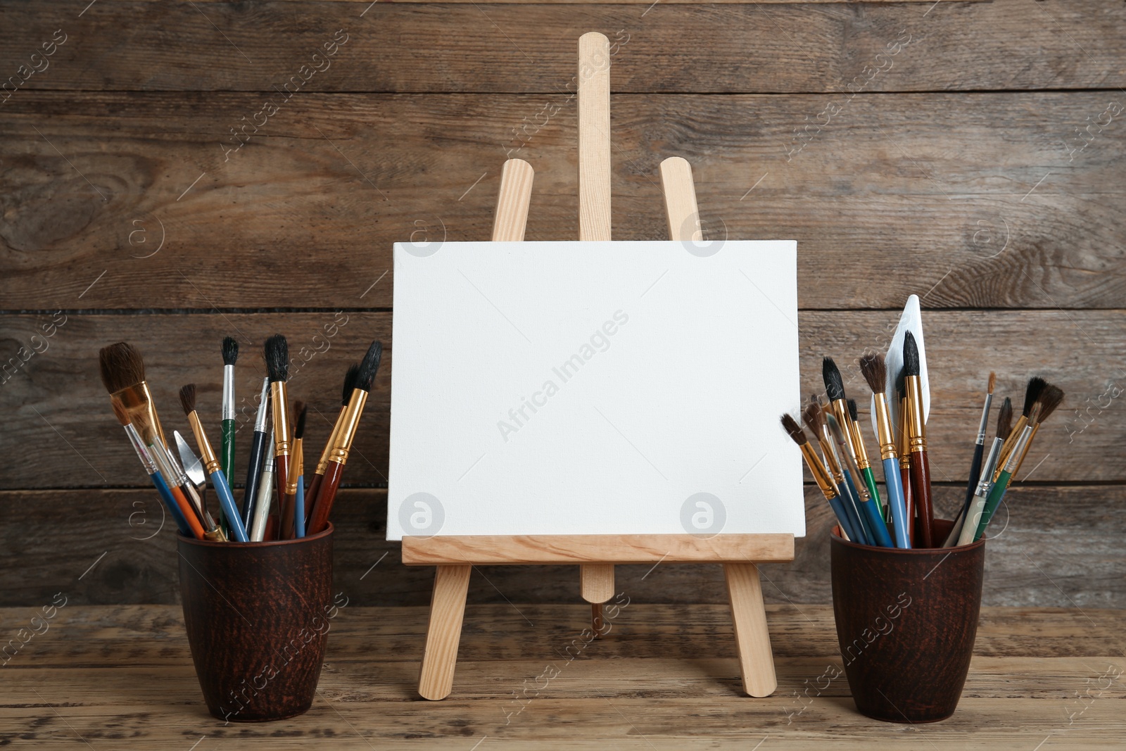 Photo of Easel with blank canvas and brushes on wooden table