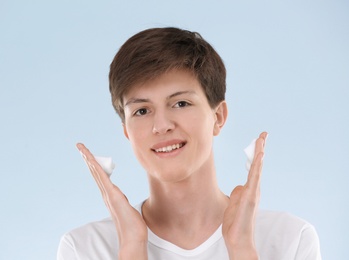 Photo of Teenage boy with problem skin applying anti acne cream on light background