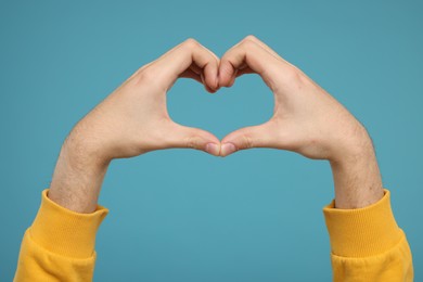 Man showing heart gesture with hands on light blue background, closeup