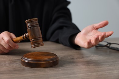 Judge with gavel sitting at wooden table against light grey background, closeup