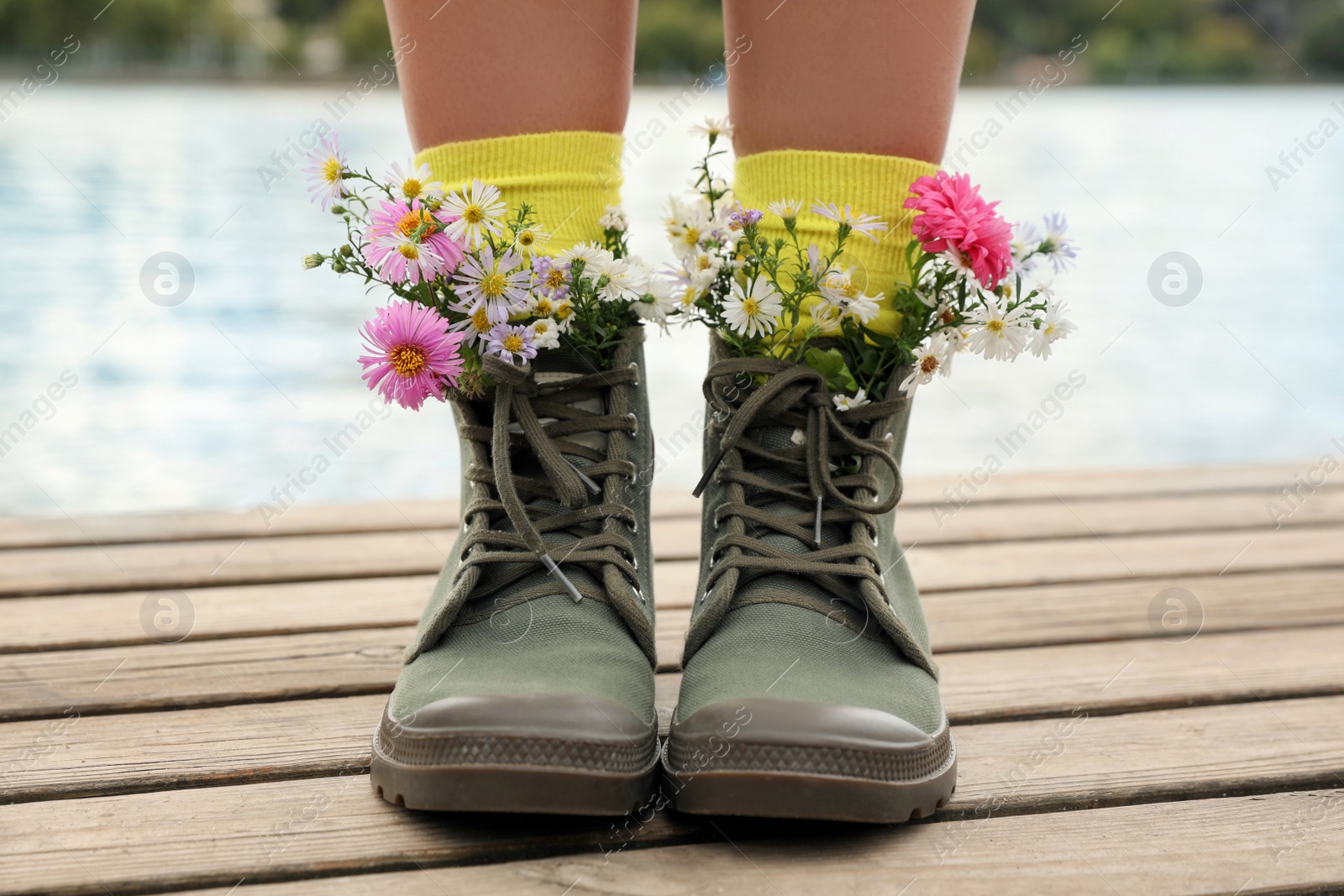 Photo of Woman with beautiful tender flowers in socks on wooden pier, closeup