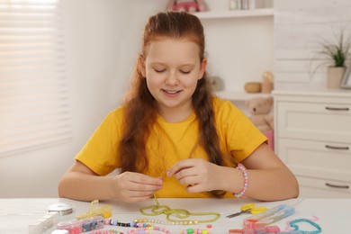 Photo of Cute girl making beaded jewelry at table in room