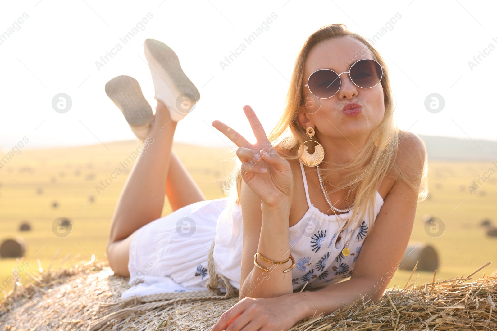 Photo of Beautiful hippie woman showing peace sign on hay bale in field