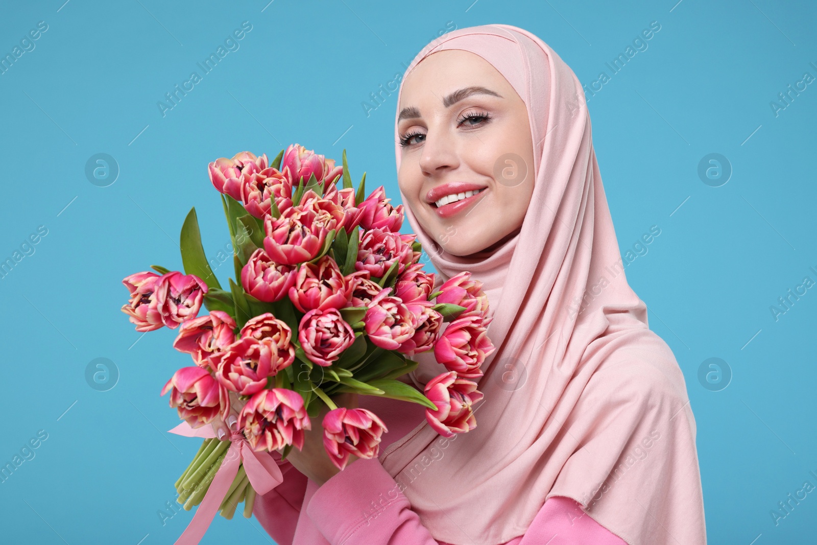 Photo of Happy woman in hijab with beautiful bouquet on light blue background