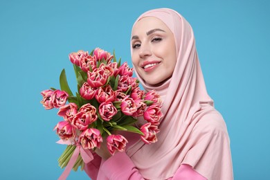 Happy woman in hijab with beautiful bouquet on light blue background