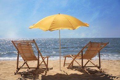 Photo of Orange beach umbrella and deck chairs on sandy seashore
