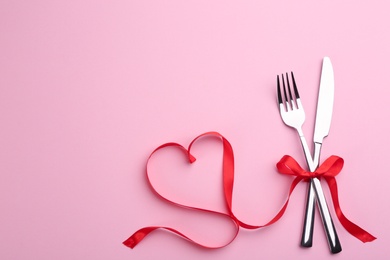 Cutlery set and red ribbon on pink background, flat lay with space for text. Valentine's Day dinner