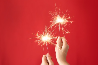Photo of Woman holding bright burning sparklers on red background, closeup