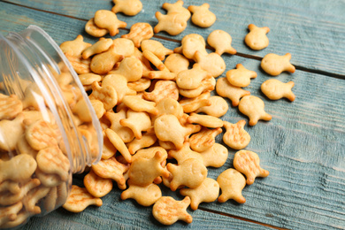Photo of Overturned jar with goldfish crackers on blue wooden table, closeup