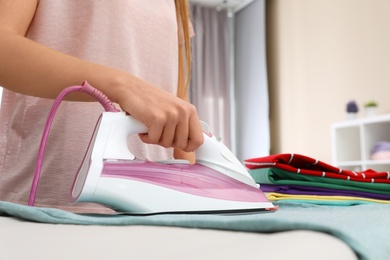 Photo of Young woman ironing clothes on board at home, closeup