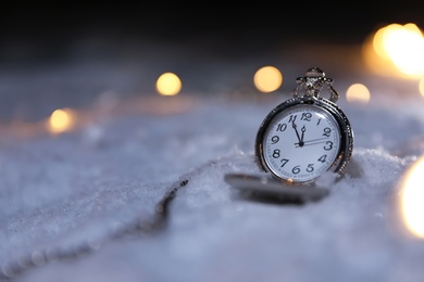 Photo of Pocket watch and Christmas lights on white snow outdoors, space for text. Midnight countdown