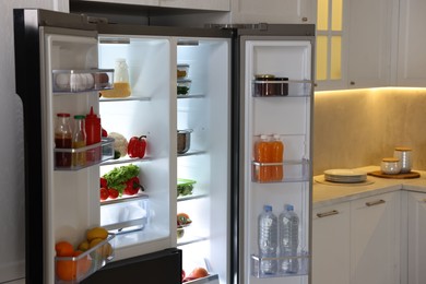 Photo of Open refrigerator full of different products in kitchen
