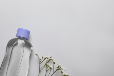Bottle of baby oil and flowers on light grey background, flat lay. Space for text