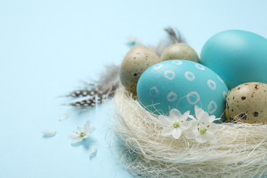 Photo of Colorful Easter eggs in decorative nest on light blue background, closeup. Space for text