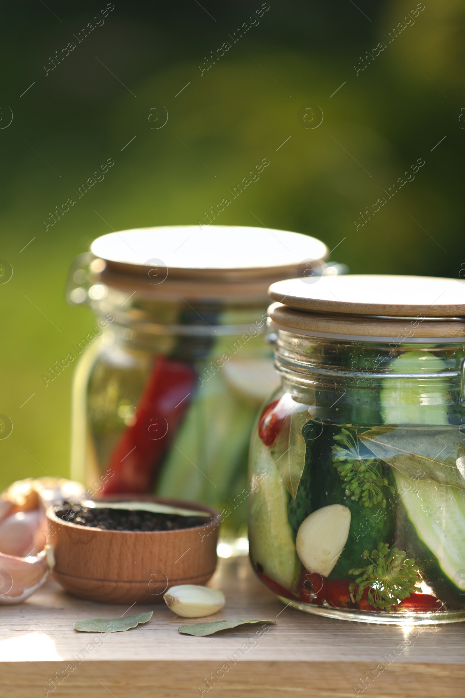 Photo of Jars of delicious pickled cucumbers and ingredients on wooden table against blurred background, closeup