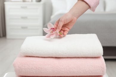 Woman putting flower on stack of clean towels in bedroom