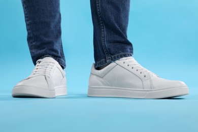 Man wearing stylish white sneakers on light blue background, closeup