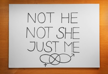 Card with text Not He Not She Just Me and gender symbols on wooden background, top view
