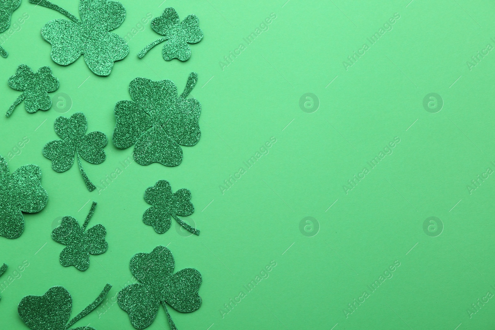 Photo of St. Patrick's day. Shiny decorative clover leaves on green background, flat lay. Space for text