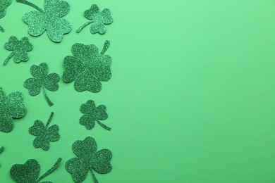 St. Patrick's day. Shiny decorative clover leaves on green background, flat lay. Space for text