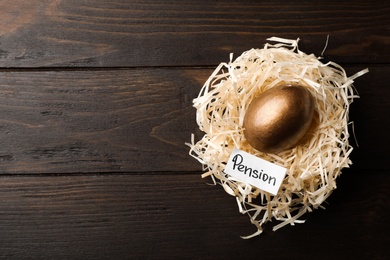 Golden egg and card with word PENSION in nest on wooden background, top view. Space for text