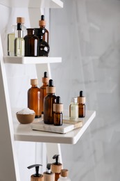 Photo of Essential oils, sea salt, and other cosmetic products on white shelving unit in bathroom
