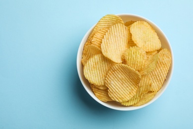 Delicious crispy potato chips in bowl on color background, top view with space for text