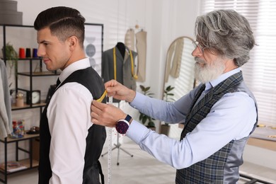 Photo of Professional tailor measuring client's back width in atelier