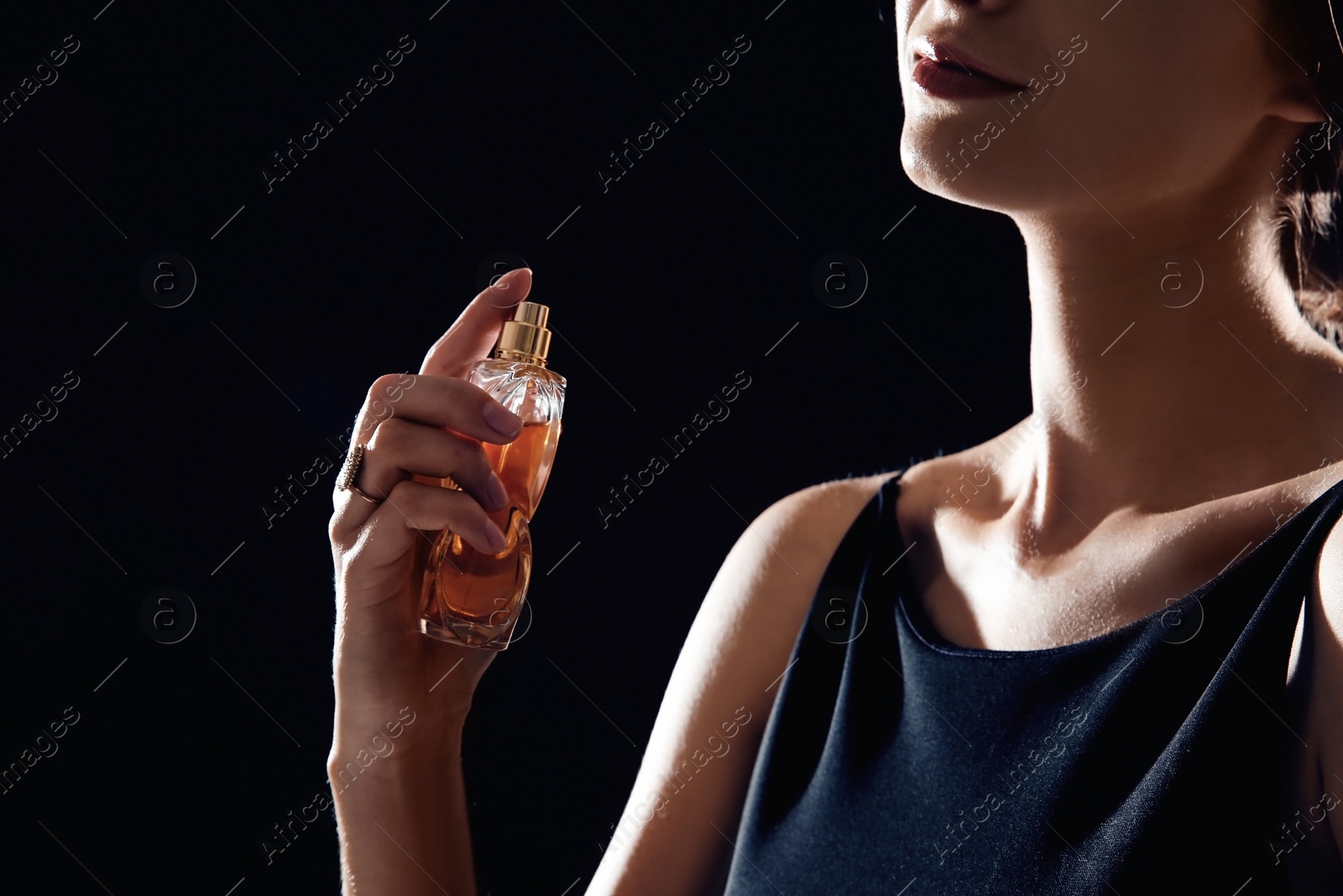 Photo of Young woman using perfume on black background, closeup