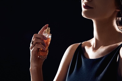 Young woman using perfume on black background, closeup