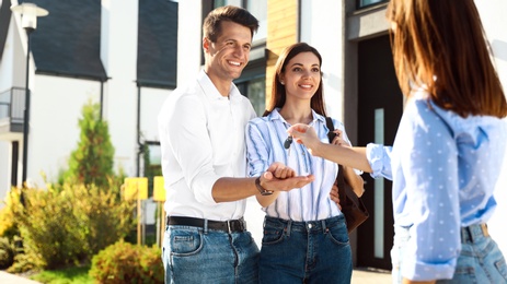 Photo of Real estate agent giving house keys to young couple outdoors