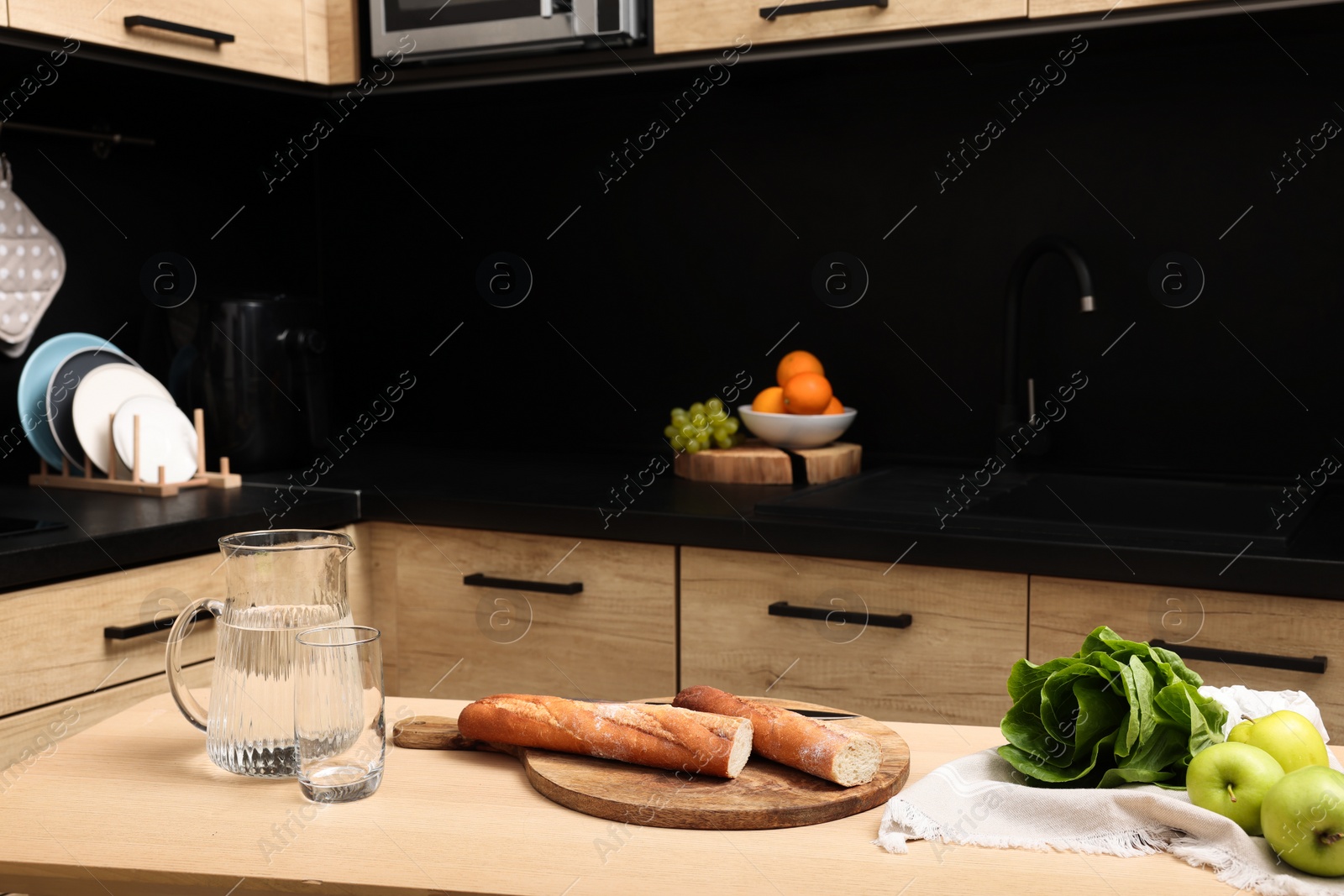 Photo of Baguettes, water glass, bok choy and green apples on table in kitchen